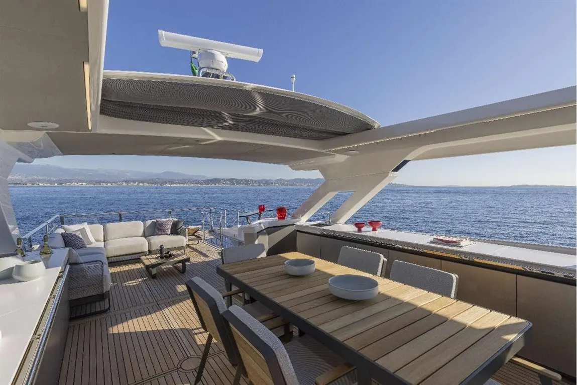 Luxury yacht deck with a dining table, lounge area, and stunning sea view under clear blue skies.